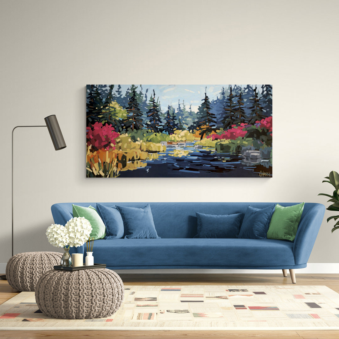 Photographie d’un salon contemporain lumineux aux tons doux et naturels. Au-dessus d’un canapé bleu velours garni de coussins assortis et verts, une grande peinture de paysage marécageux est accrochée au mur crème. L’œuvre représente un marais paisible bordé de conifères sombres et de végétation colorée dans des tons rouges, dorés et verts, se reflétant dans une eau calme sous une lumière matinale. Des poufs tricotés, une lampe minimaliste noire et quelques plantes complètent l’ambiance chaleureuse et moder
