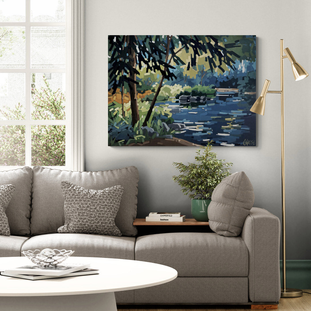 Peinture contemporaine de paysage représentant un lac paisible au crépuscule, présentée dans un salon moderne et lumineux. Les reflets dorés sur l'eau, les arbres et la végétation évoquent le calme d'une fin de journée estivale et illustrent l'intégration de l'œuvre dans un décor contemporain.