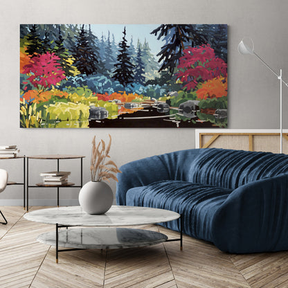 Peinture paysagère contemporaine représentant un paisible ruisseau forestier bordé de rochers et d'une végétation lumineuse aux teintes d'automne. Des arbustes rouge carmin et orangés encadrent l'eau calme qui reflète la lumière, tandis qu'une forêt de conifères bleu-gris s'élève à l'arrière-plan dans une douce atmosphère brumeuse. L'œuvre est présentée au-dessus d'un canapé bleu dans un salon au style contemporain chaleureux.